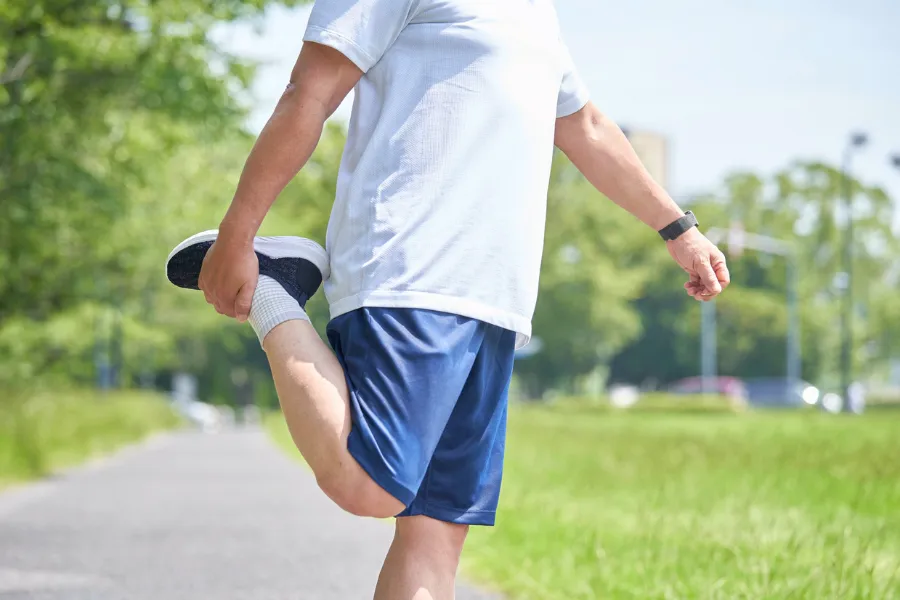 Man on outdoor trail in athletic clothing stretching leg for a jog or run